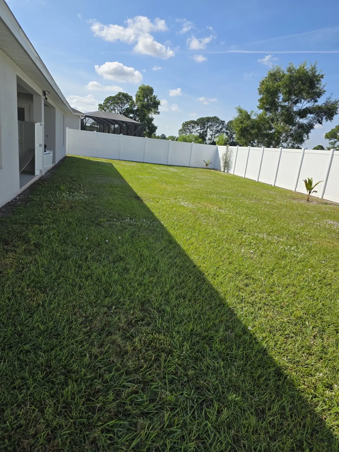 Large fenced backyard with green lawn and open sky