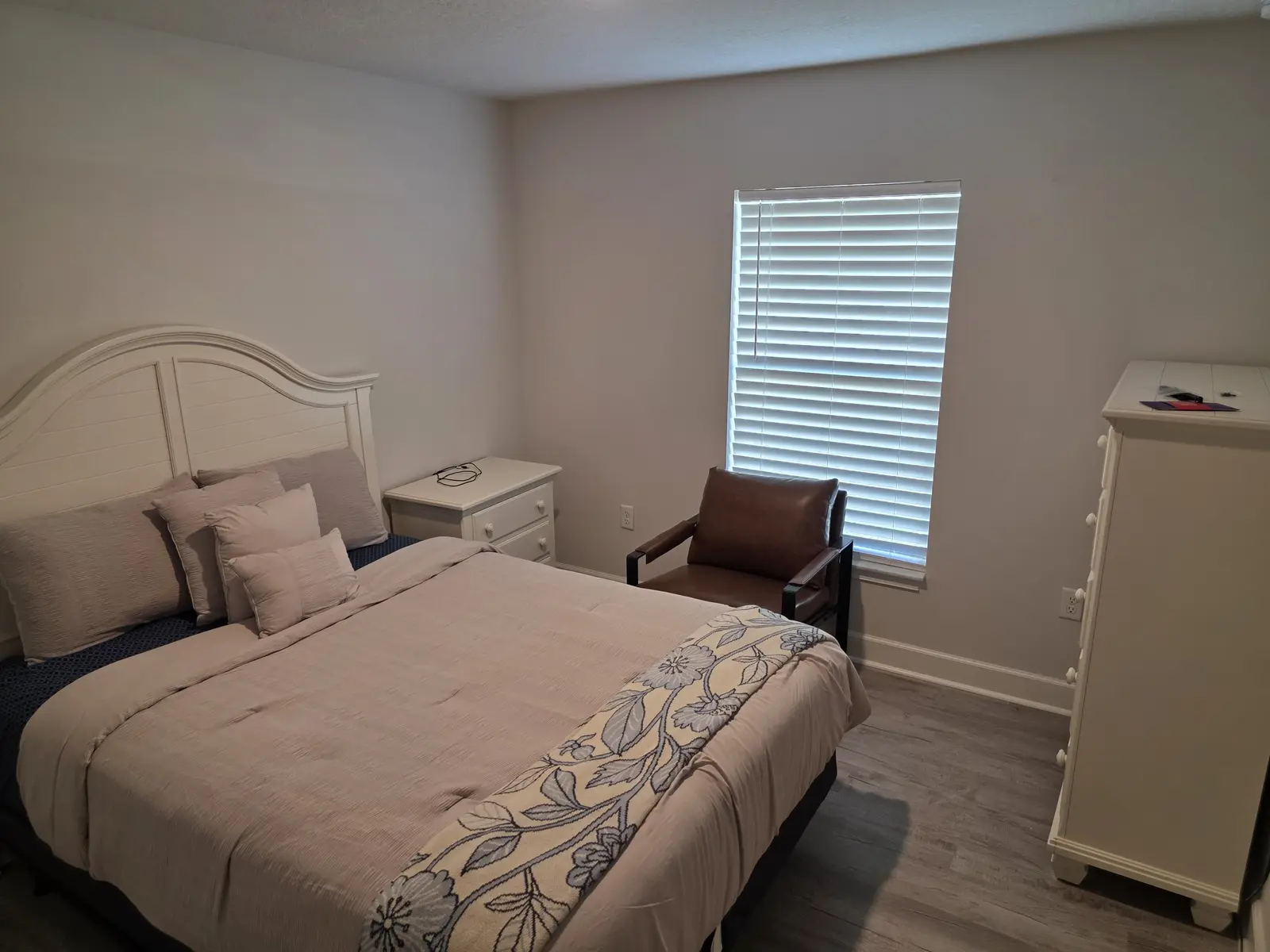 Comfortable private bedroom with white bed, dresser, chair and natural light