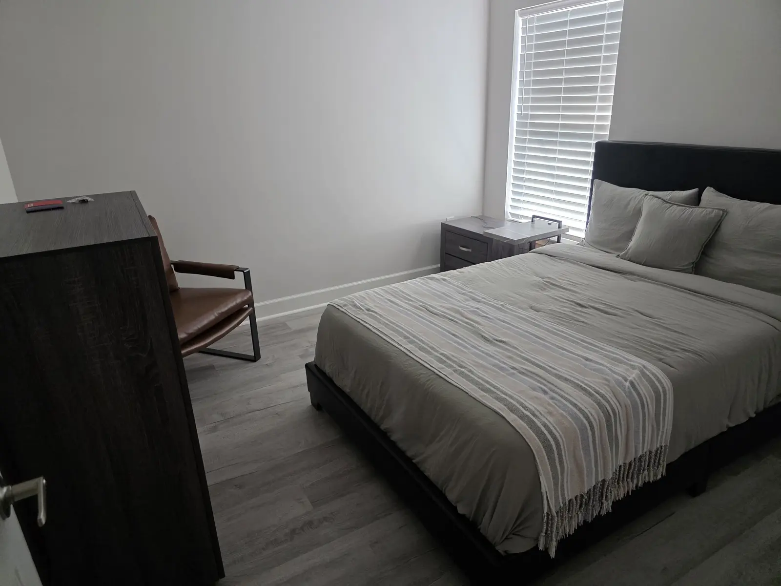 Bright private bedroom with upholstered bed, dresser, chair and window