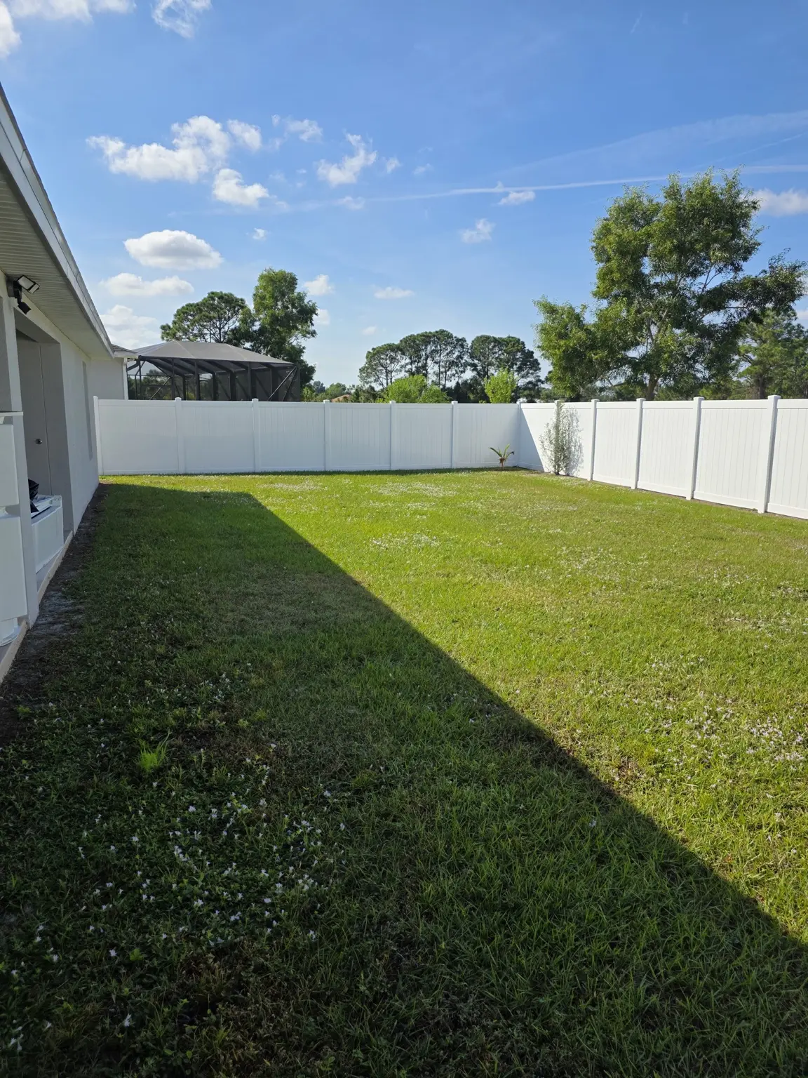 Wide view of the large fenced backyard with green lawn and blue sky